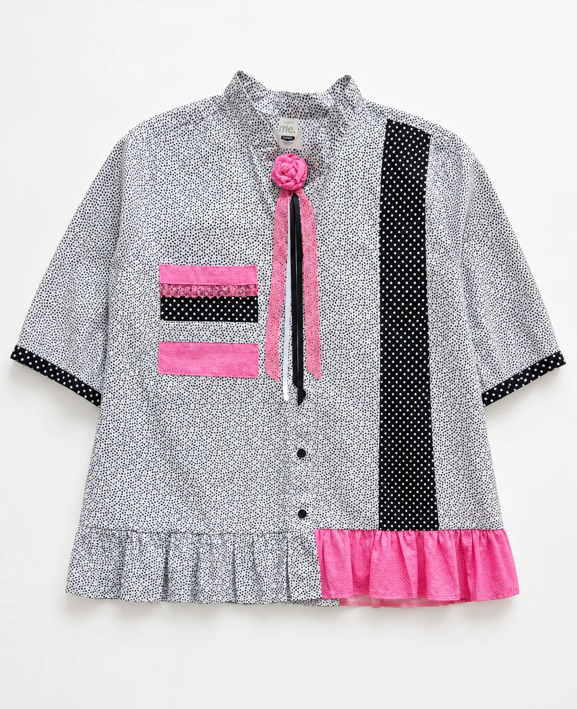 Dolly — black and white micro-print blouse with polka dot panel, pink accents, ruffled hem and pink flower at neckline, flat lay
